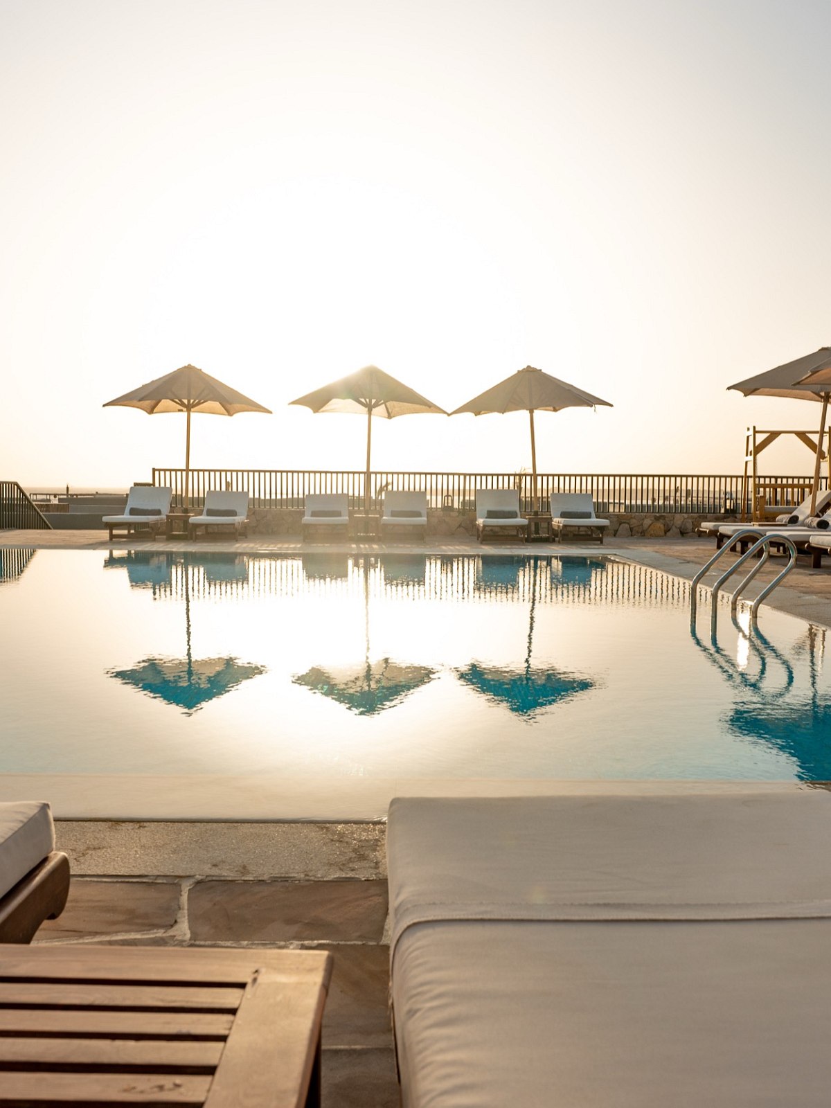 Ein Pool mit Liegen und Sonnenschirm, im Hintergrund der Sonnenuntergang